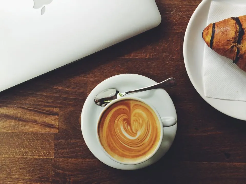 A latte with leaf art beside a croissant