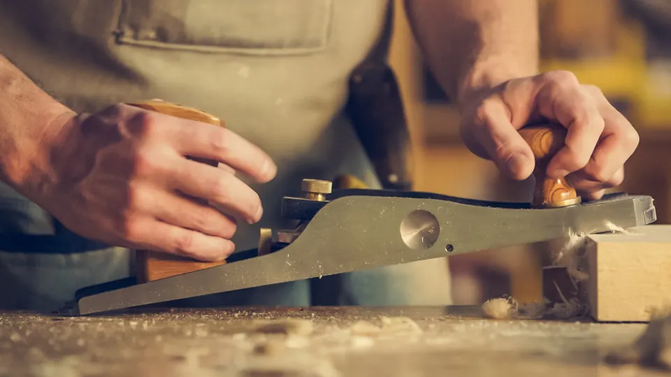 A carpenter's hands guiding a hand plane along a board