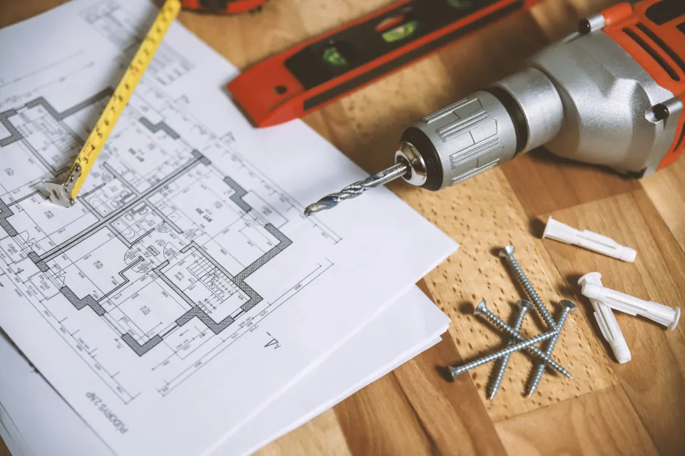 House plans on a workbench with a drill, level and tape measure
